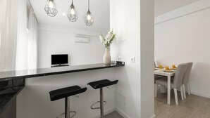 A modern kitchen with a black countertop, two bar stools, a flat-screen TV, and pendant lights. - Nazaré Horizon - Balcony View (Nazaré)