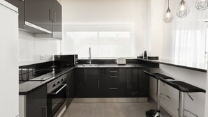 A modern kitchen with black cabinets, stainless steel appliances, a large window, and a bar stool. - Nazaré Horizon - Balcony View (Nazaré)