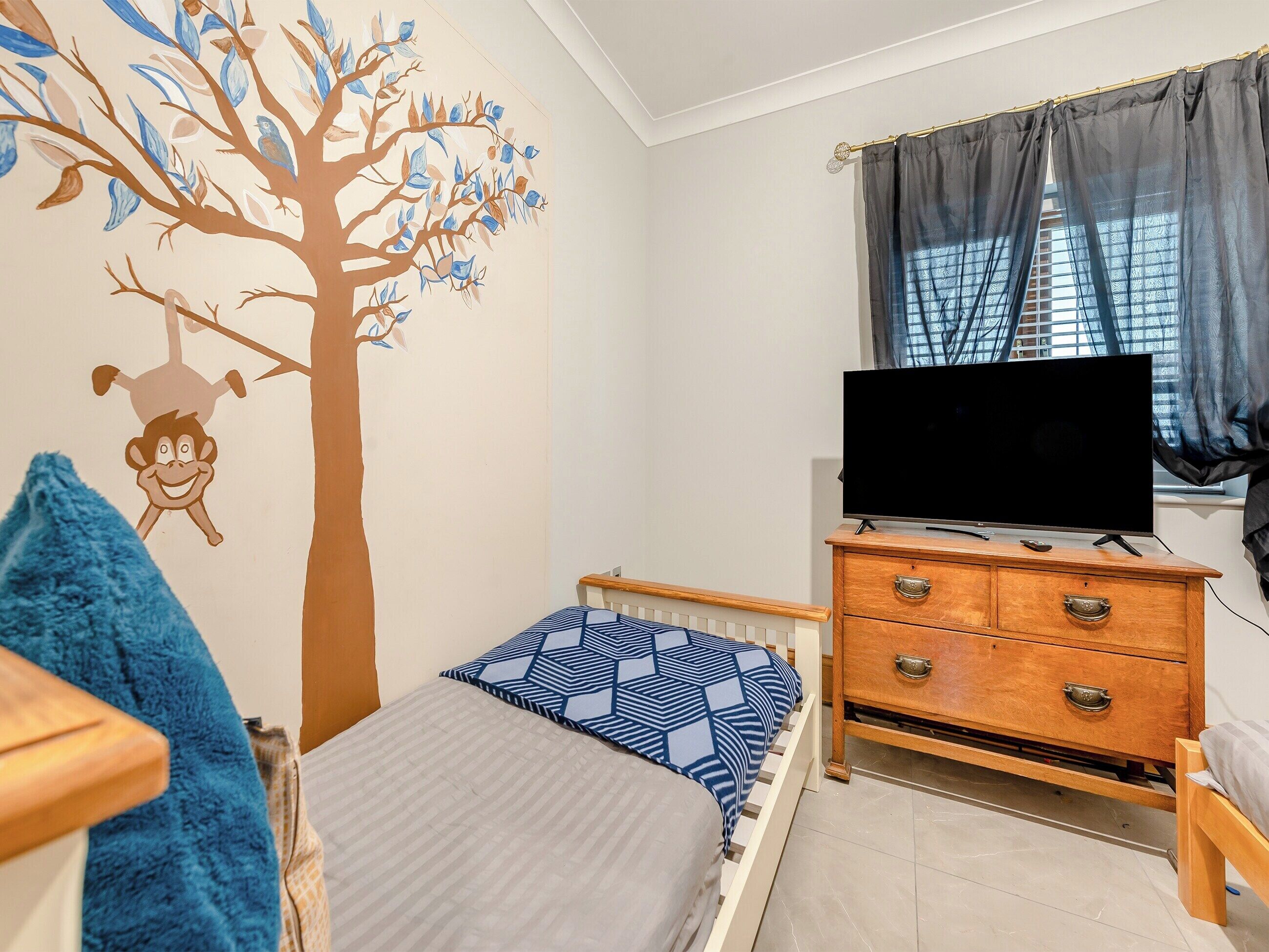 A bedroom with a bed, a dresser, a TV, and a window with curtains.