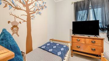 A bedroom with a bed, a dresser, a TV, and a window with curtains.