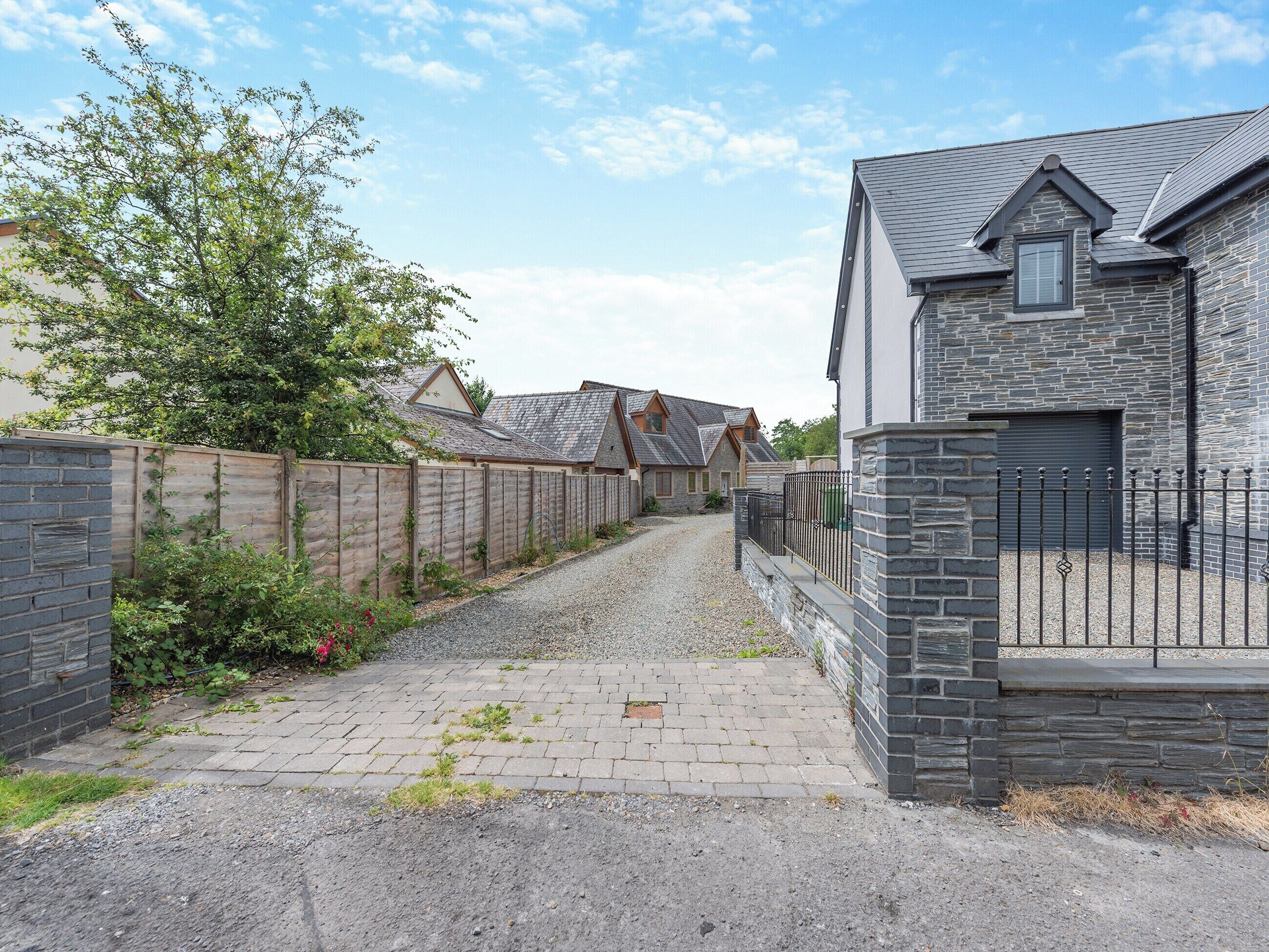 A residential street with houses, a gravel driveway, and a wooden fence.