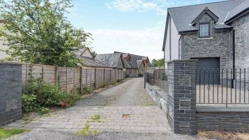 A residential street with houses, a gravel driveway, and a wooden fence.