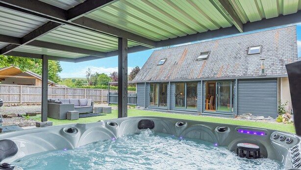 Un área de jacuzzi con un patio cubierto, una terraza de madera y una casa al fondo.
