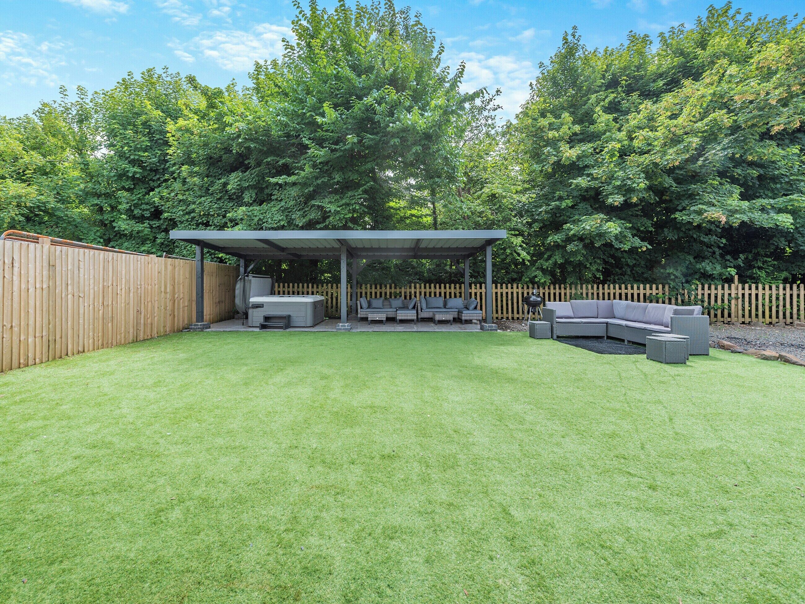 A backyard with a covered patio area, outdoor seating, and a wooden fence.