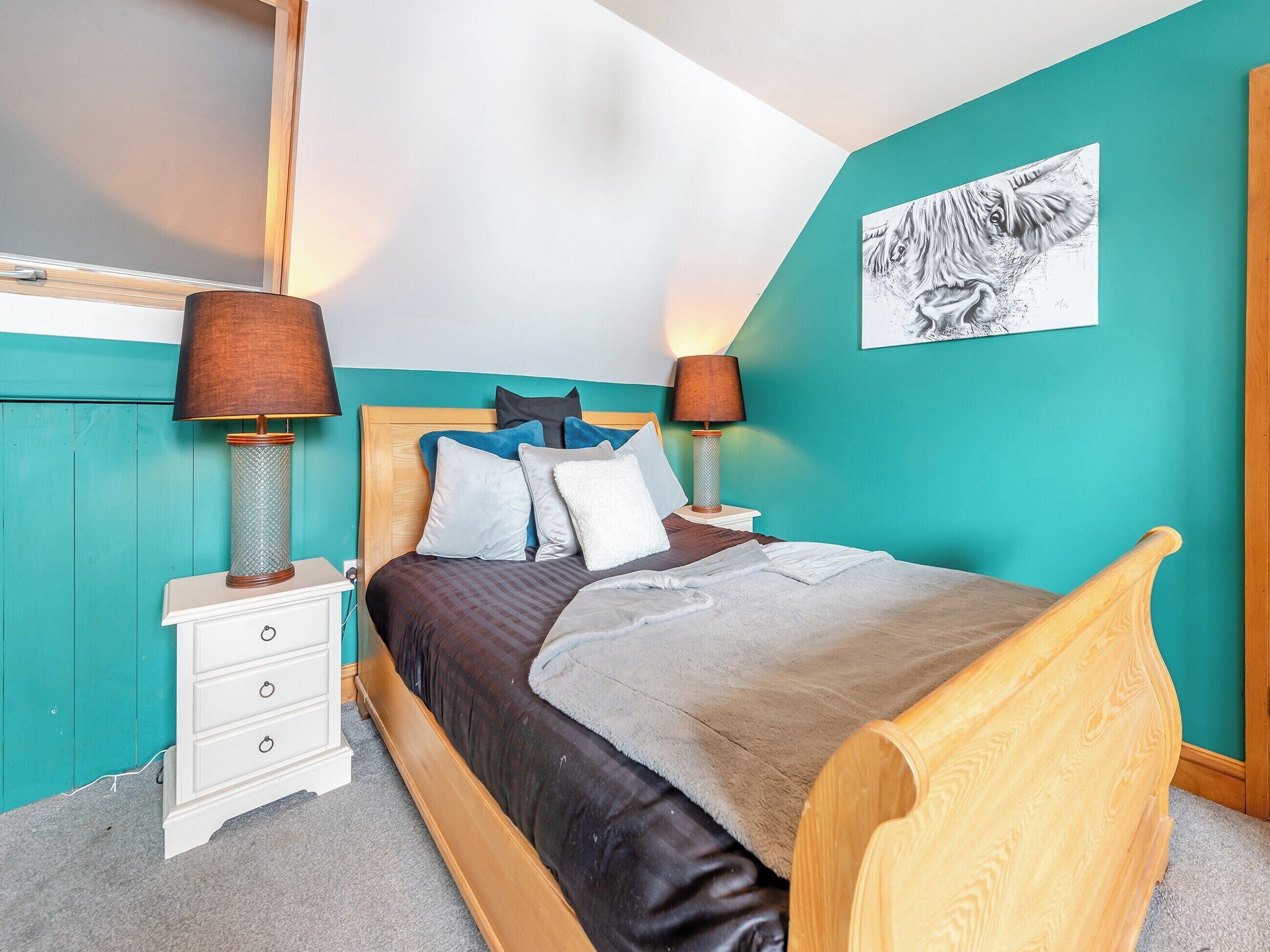 A bedroom with a wooden bed, teal walls, and a black and white artwork on the wall.