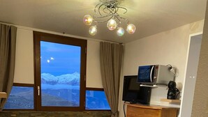 A hotel room with a bed, a massage chair, a television, and a view of snow-capped mountains through the window. - Studio Corbier Zodiaque Pool and Ski at the foot of the slopes  (Villarembert)