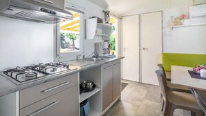 Eine kleine Küche mit einer Gaskochstelle, einem Spülbecken und einem Fenster. Es gibt eine Essecke mit Tisch und Stühlen.