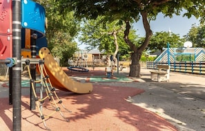 Explore the playground area with a slide and climbing frames, surrounded by trees and a seating bench.
