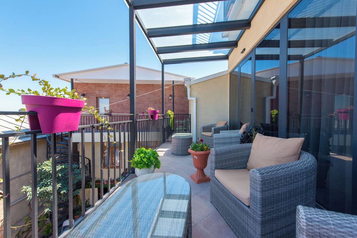An outdoor patio with wicker furniture, potted plants, and a glass ceiling.