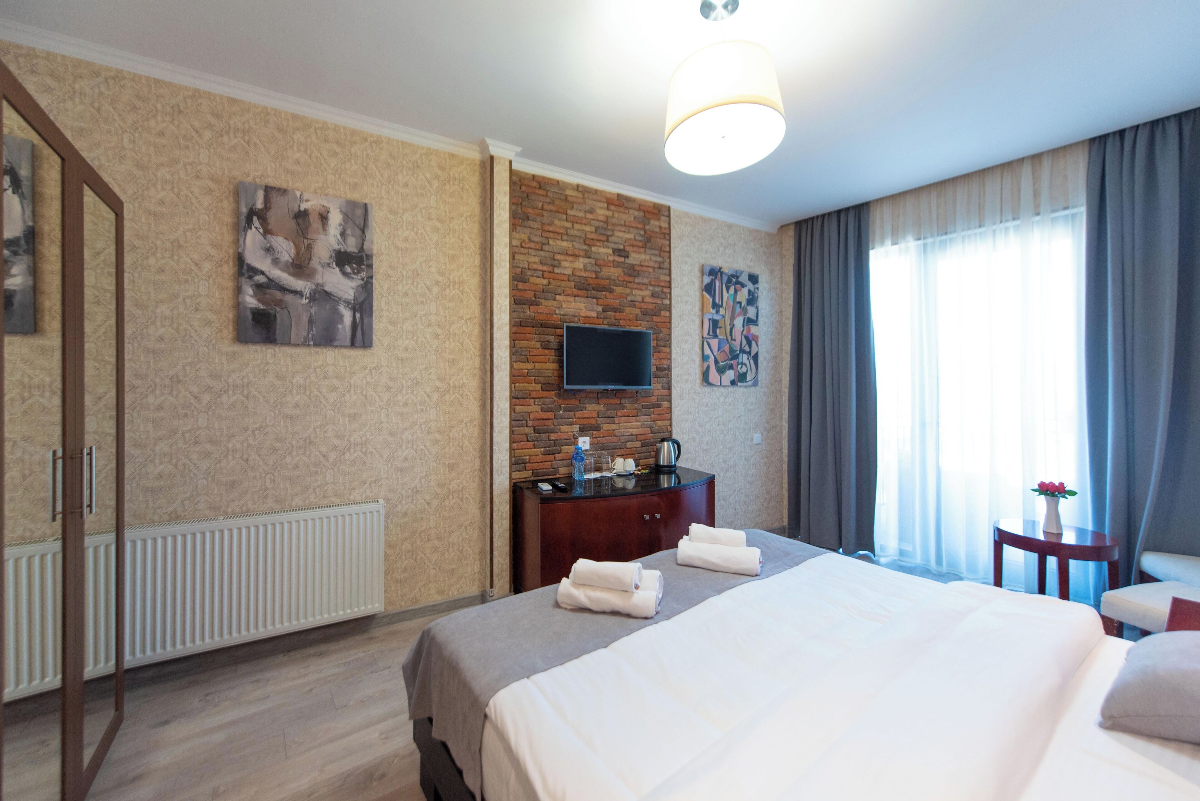 A hotel room with a bed, a TV, a dresser, and a window with curtains.