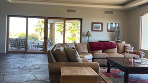 A spacious living room with a large sofa, a coffee table, and a view of a patio with outdoor furniture and palm trees. - 100 mile views! 6000 sq ft 4-bedroom house, salt pool in fabulous Fountain Hills (Fountain Hills)