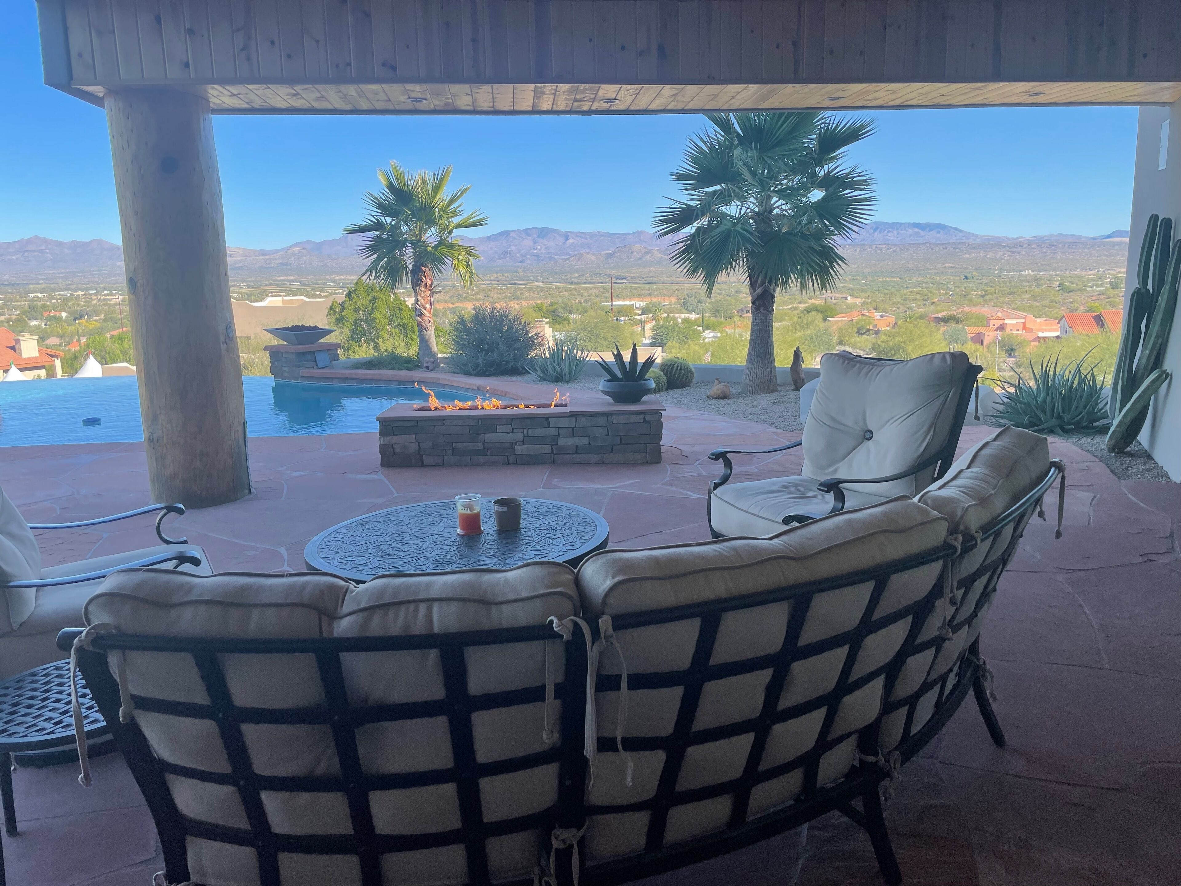 A covered patio with outdoor seating, a pool, and a view of mountains and houses.