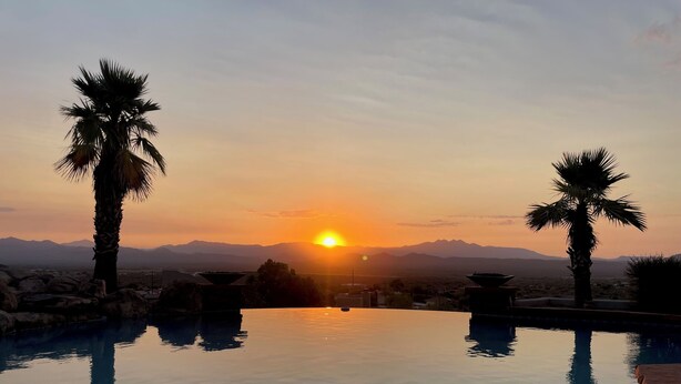 A serene sunset view over a calm pool with palm trees, surrounded by mountains. - 100 mile views! 6000 sq ft 4-bedroom house, salt pool in fabulous Fountain Hills (Fountain Hills)