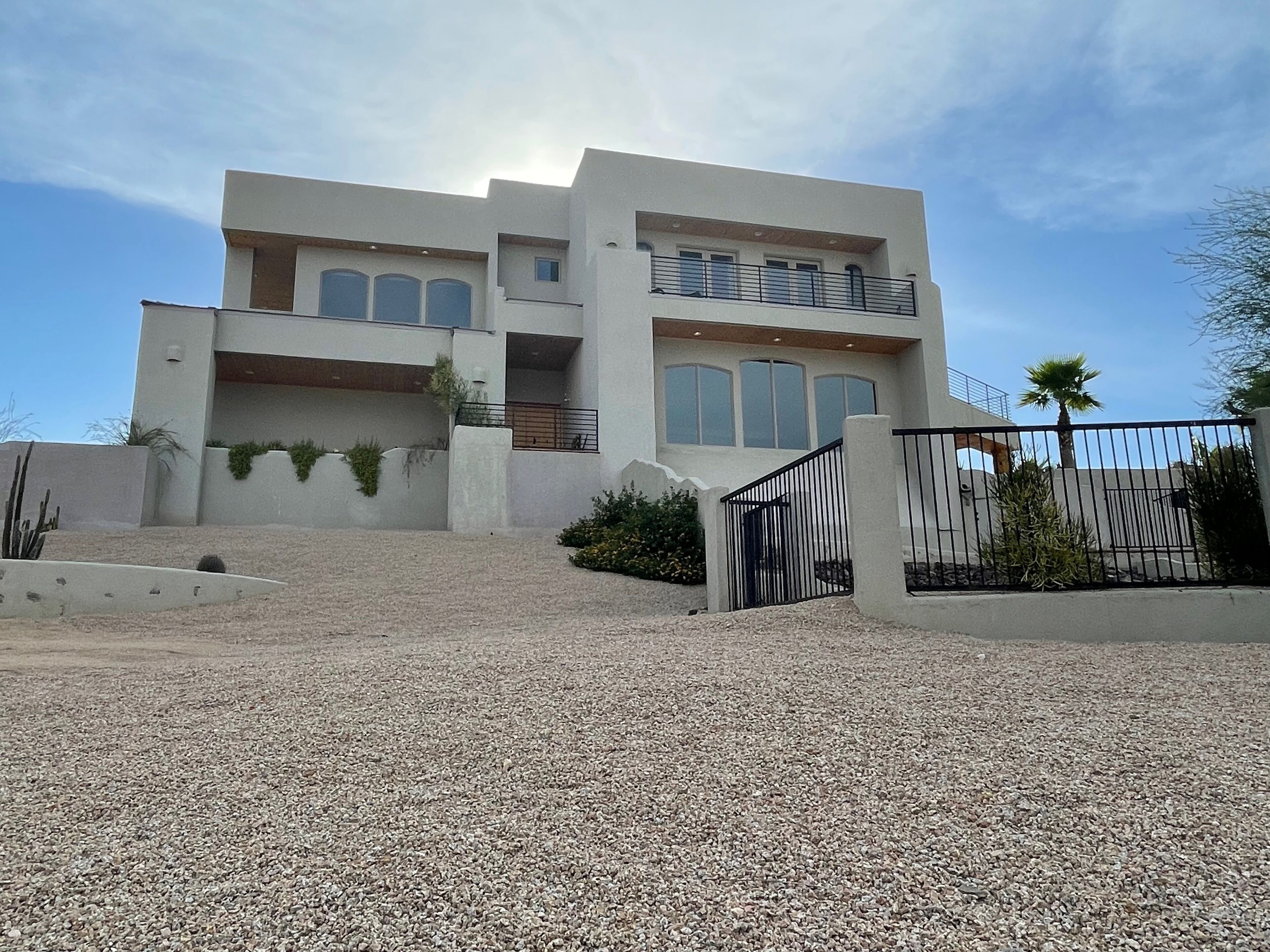 Uma casa moderna de dois andares com entrada por um portão e acesso por um caminho de pedras.