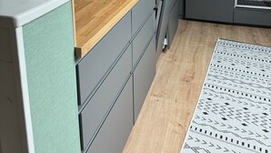 Una cocina moderna con encimera de madera, armarios grises, una lámpara colgante negra y una ventana con persianas.