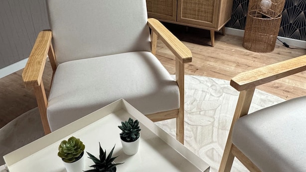 Una sala de estar moderna con un sillón blanco, una mesita pequeña con plantas en macetas, un mueble de madera y una pared con diseño.