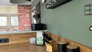Una cocina con encimera de madera, una lámpara colgante negra, una pared de ladrillo decorativa y un estante con utensilios de cocina.