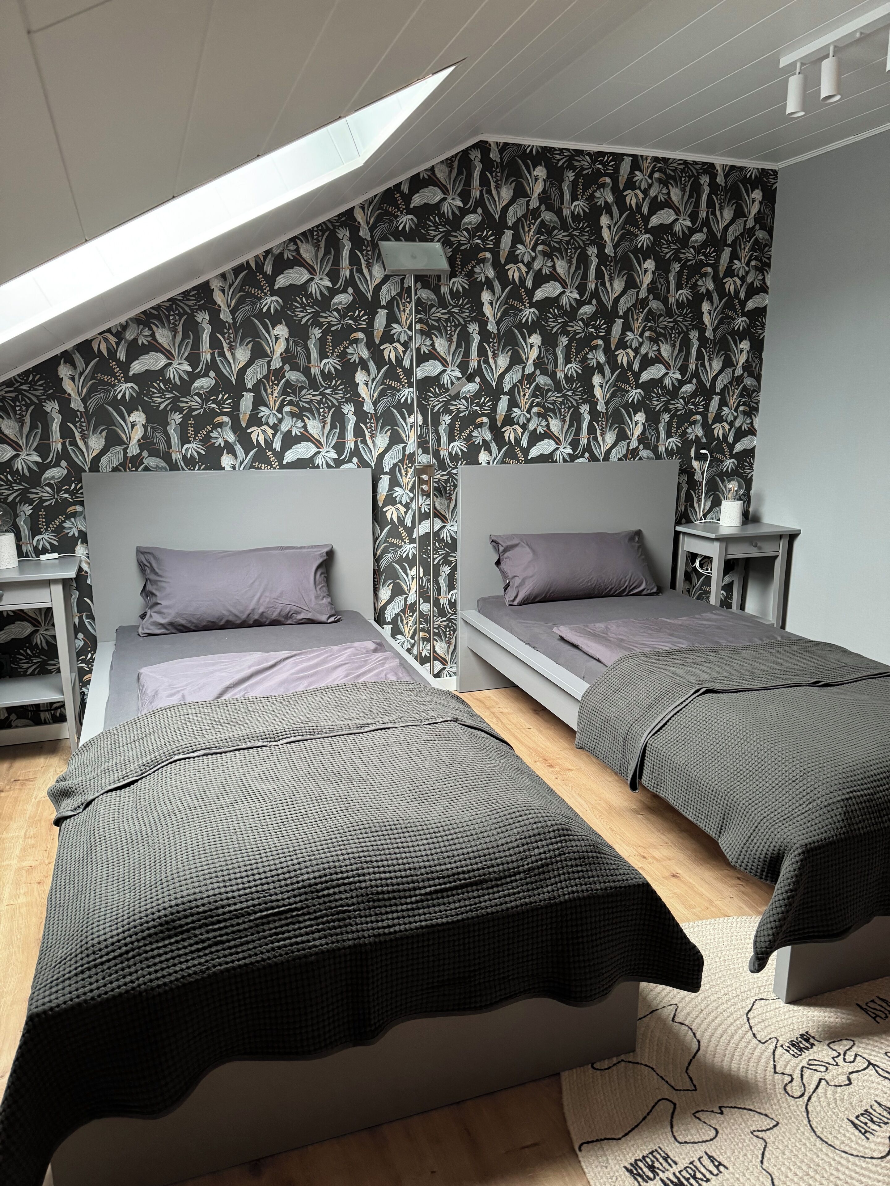A bedroom with two beds, a skylight, and a floral wallpaper.