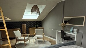 Un dormitorio estilo loft moderno con techo inclinado, tragaluces, cama con cubrecama blanco acolchado, escritorio con silla y escalera de madera.