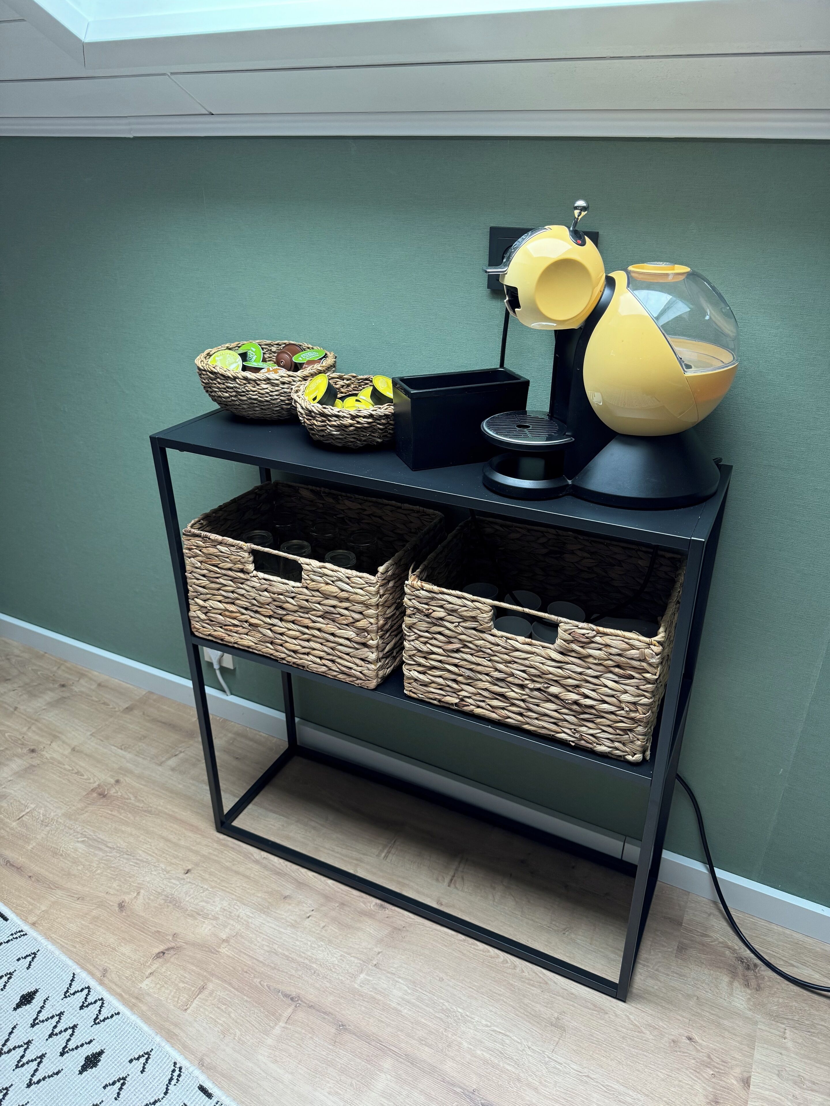 A black metal table with woven baskets and a yellow lamp against a green wall.