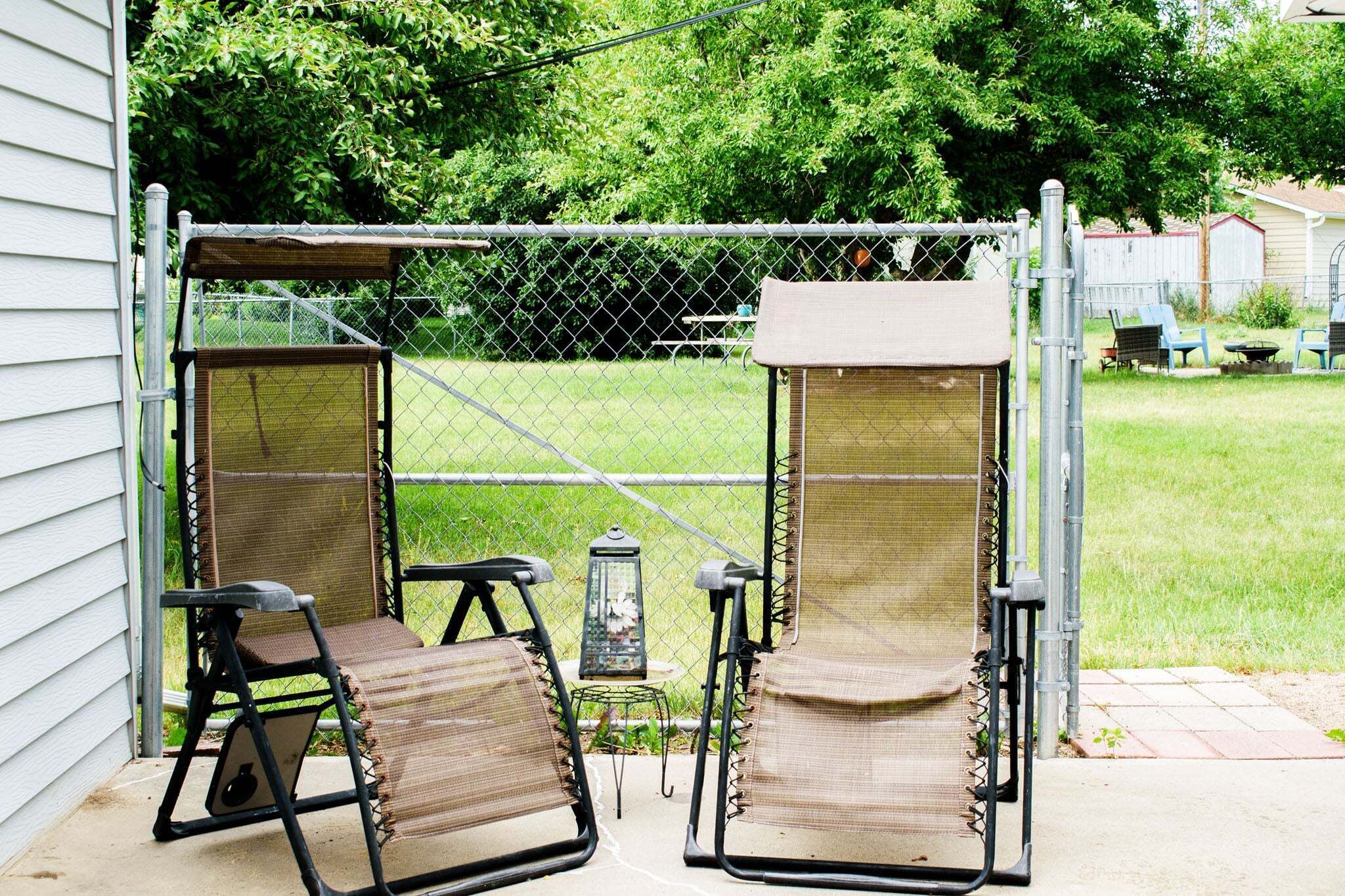 A covered outdoor seating area with two chairs and a table, enclosed by a chain-link fence.