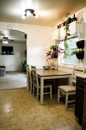A dining area with a wooden table, six chairs, a ceiling fan, and hanging plants.
