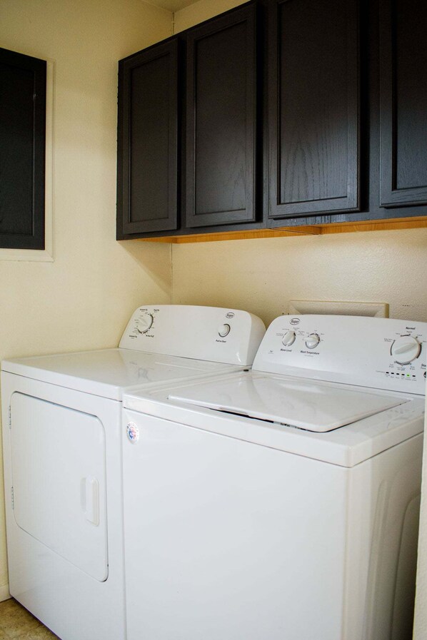 A laundry area with a front-loading washer and dryer, dark cabinets above, and a beige wall.