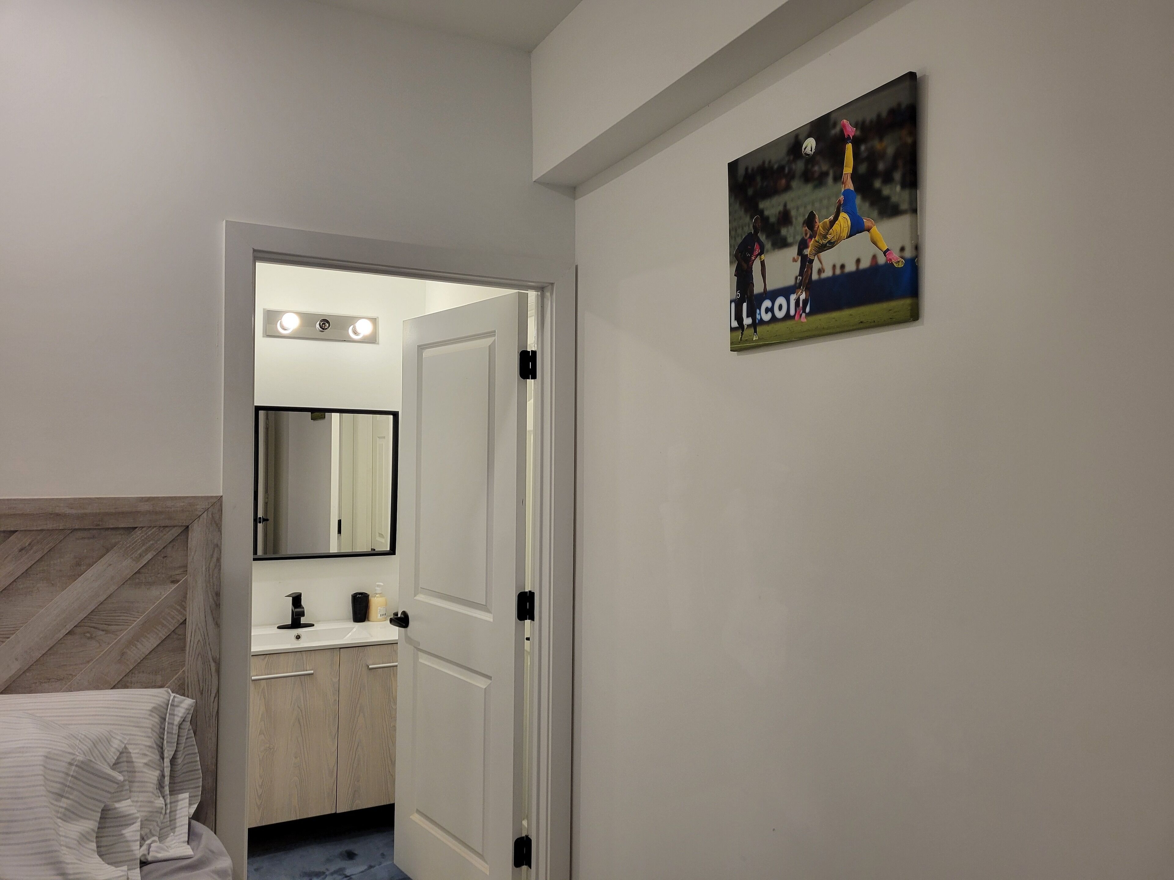 Habitación de hotel con una cama, un espejo, un lavamanos y una puerta que da a un baño.