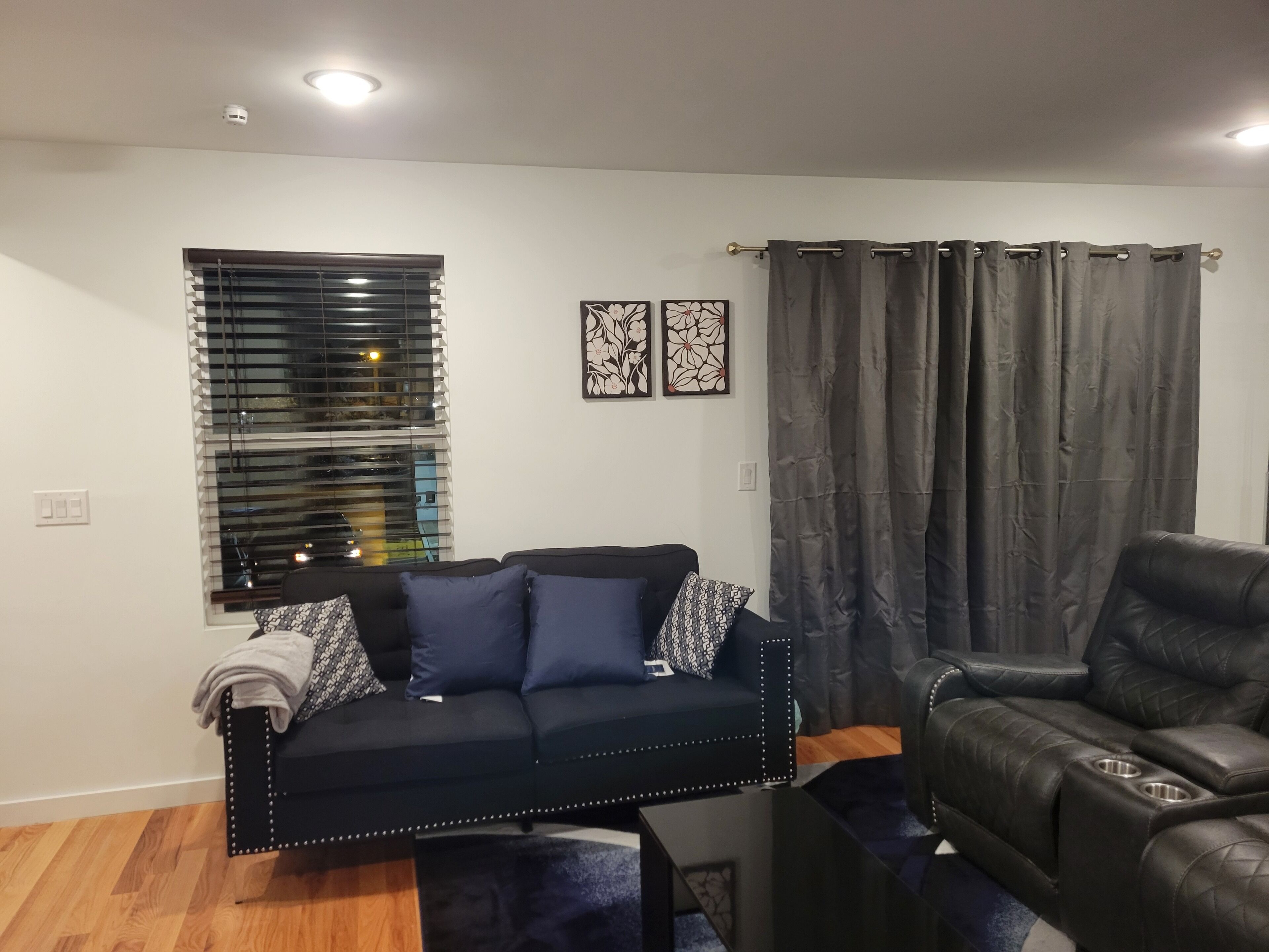 A living room with a black sofa, a black leather chair, a window with blinds, and a curtain.