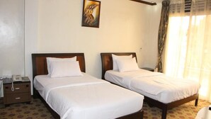 A hotel room with two single beds, a bedside table with a phone, and a window with curtains. - Karibu Stay (Muhoza)