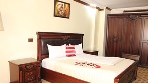 A neatly made bed with a wooden headboard, a bedside table with drawers, and a wardrobe. - Karibu Stay (Muhoza)