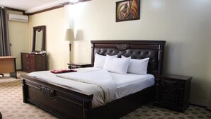 A neatly made bed with a dark headboard, a bedside table, a dresser, and a wall-mounted mirror. - Karibu Stay (Muhoza)