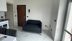 Ein modernes Wohnzimmer mit einem dunklen Sofa, einer Holztür und einer weißen Wand mit einem kleinen schwarzen Schalter.