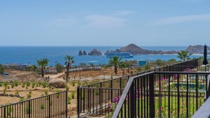 A coastal view with a clear sky, a rocky outcrop, and a pool area with a fence.