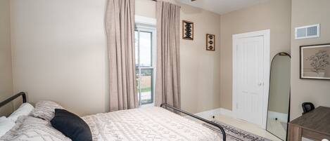 A bedroom with a bed, a ceiling fan, a window with curtains, a door, and a mirror.