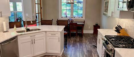 A kitchen with white cabinets, a wooden floor, a gas stove, and a window with a view of greenery.