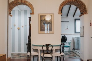 A dining area with a round table, two chairs, a framed artwork above the table, and brick arches framing the space.