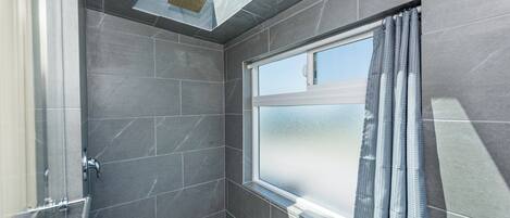 Une salle de bain moderne dotée d’un puits de lumière, d’une grande fenêtre à vitrage dépoli et d’un espace douche.