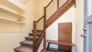 Un escalier avec des marches en bois et une rampe en métal, menant à une porte dotée d’un panneau en bois.
