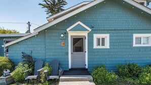 Une maison bleue avec une porte d’entrée, deux fenêtres et un petit porche agrémenté de fauteuils Adirondack.