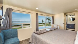 Une chambre à coucher avec un grand lit, une chaise, une coiffeuse avec un miroir et une vue sur une étendue d’eau par la fenêtre.