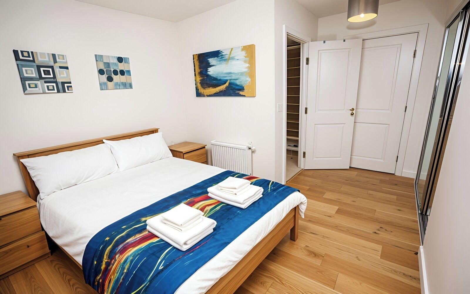 A bedroom with a wooden bed, white bedding, a colorful abstract painting, and a white radiator.