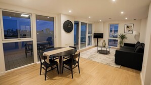 A modern living room with a dining area, a black sofa, a round table, and a large window.