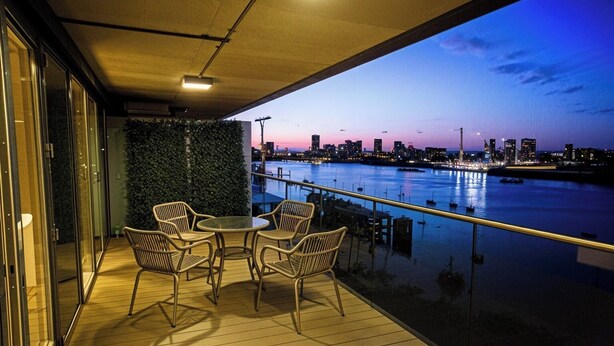 A balcony with a view of a city skyline at dusk, featuring a table and chairs.