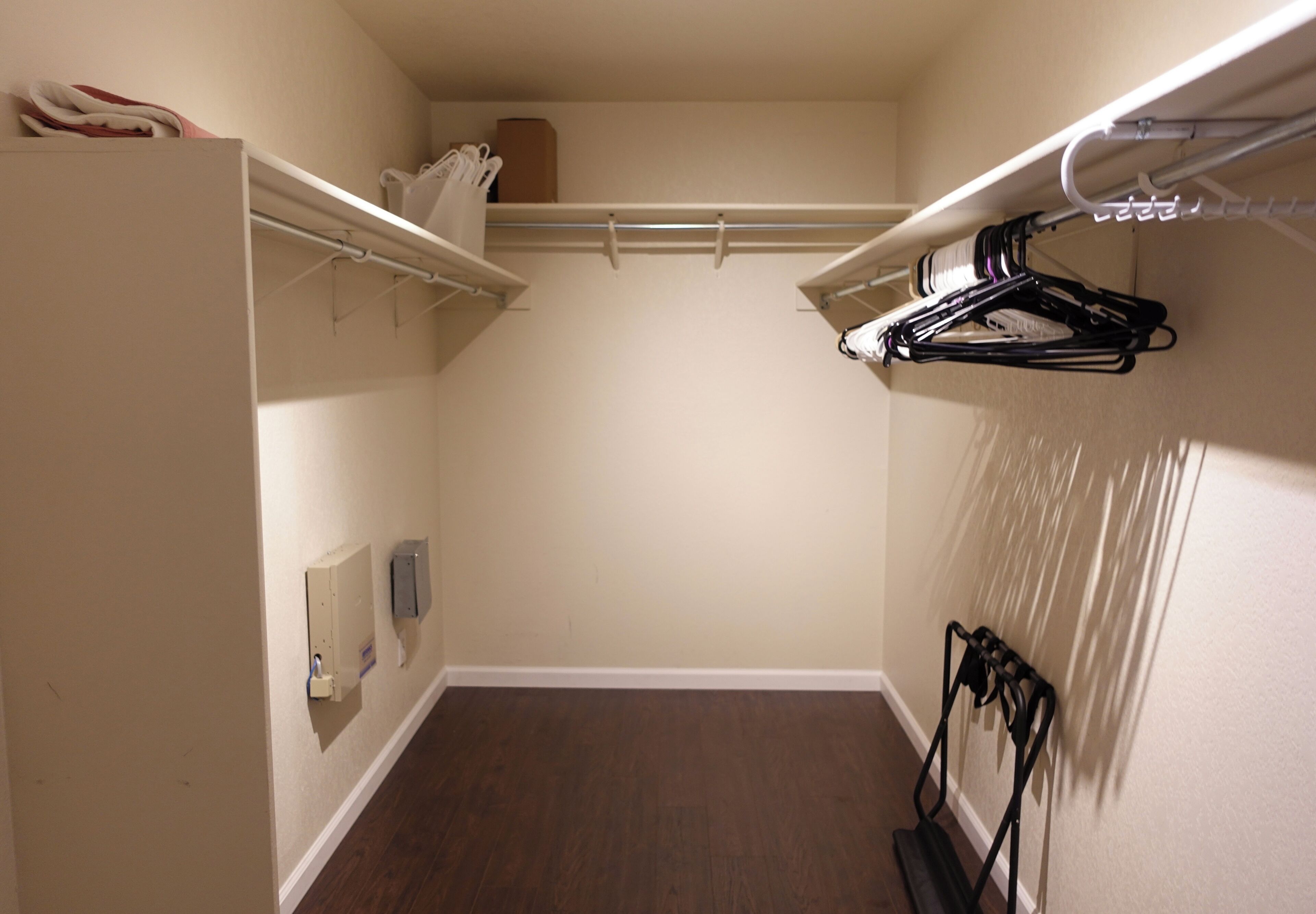 Et rum med walk-in-garderobe, trægulv, hvide vægge og et hvidt loft.