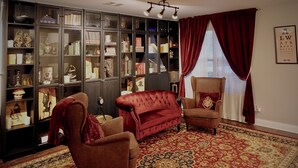 Een woonkamer met een rode bank, een bruine fauteuil, een grote boekenkast en een kamerbreed tapijt met dessin.