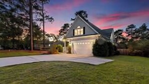 A house with a garage, surrounded by a well-maintained lawn and trees. - Relaxing home w/ putting green 5 min to Pinehurst (Pinehurst)