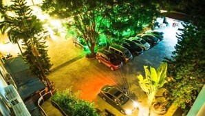 An aerial view of a parking area with several cars, surrounded by trees and greenery. - Xinhe Business Hotel (Yingjiang)