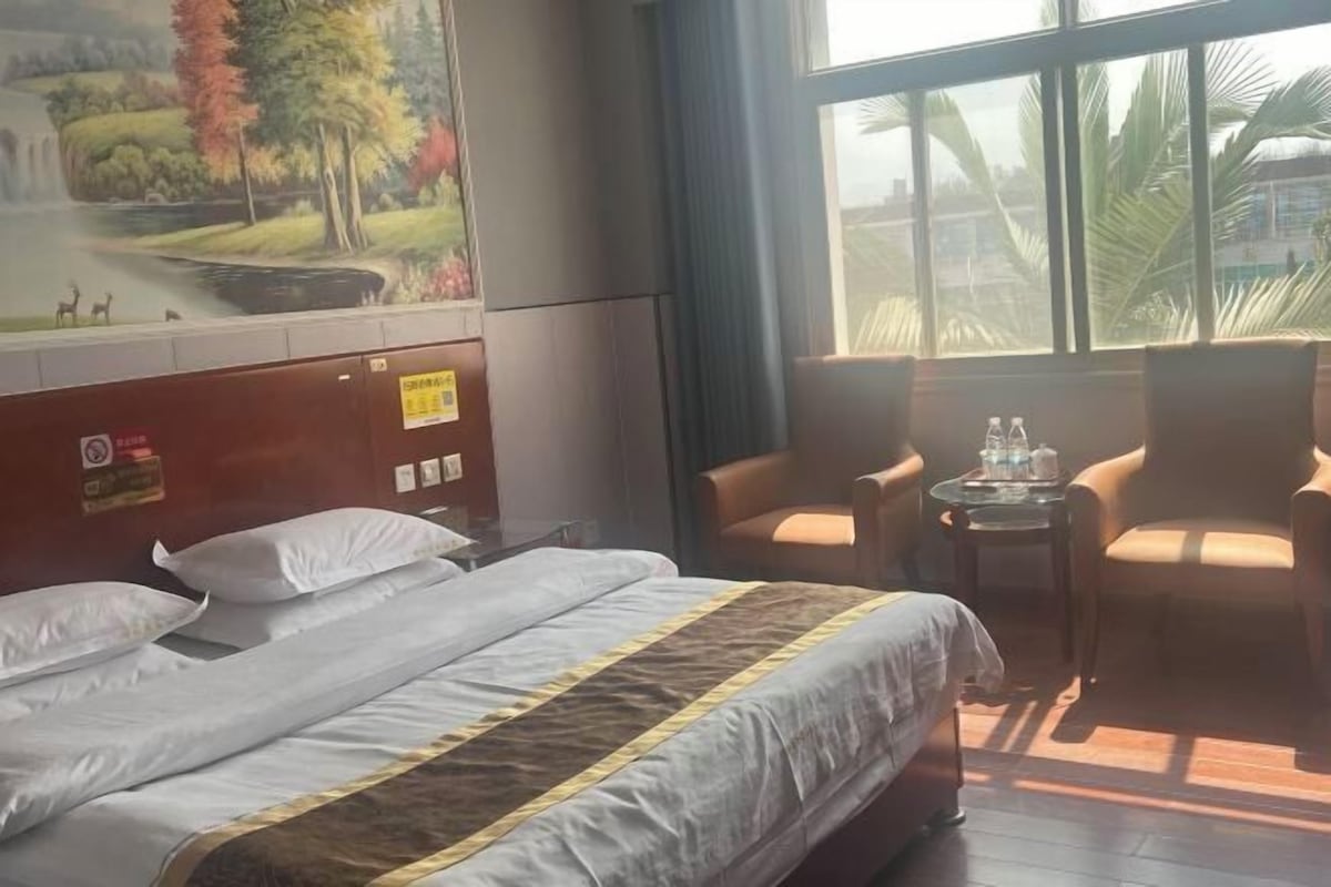 A hotel room with a bed, two armchairs, a small table with water bottles, and a mural of a landscape on the wall.