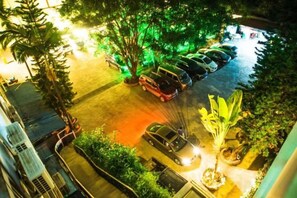 Un estacionamiento con varios autos, un árbol y un edificio al fondo.